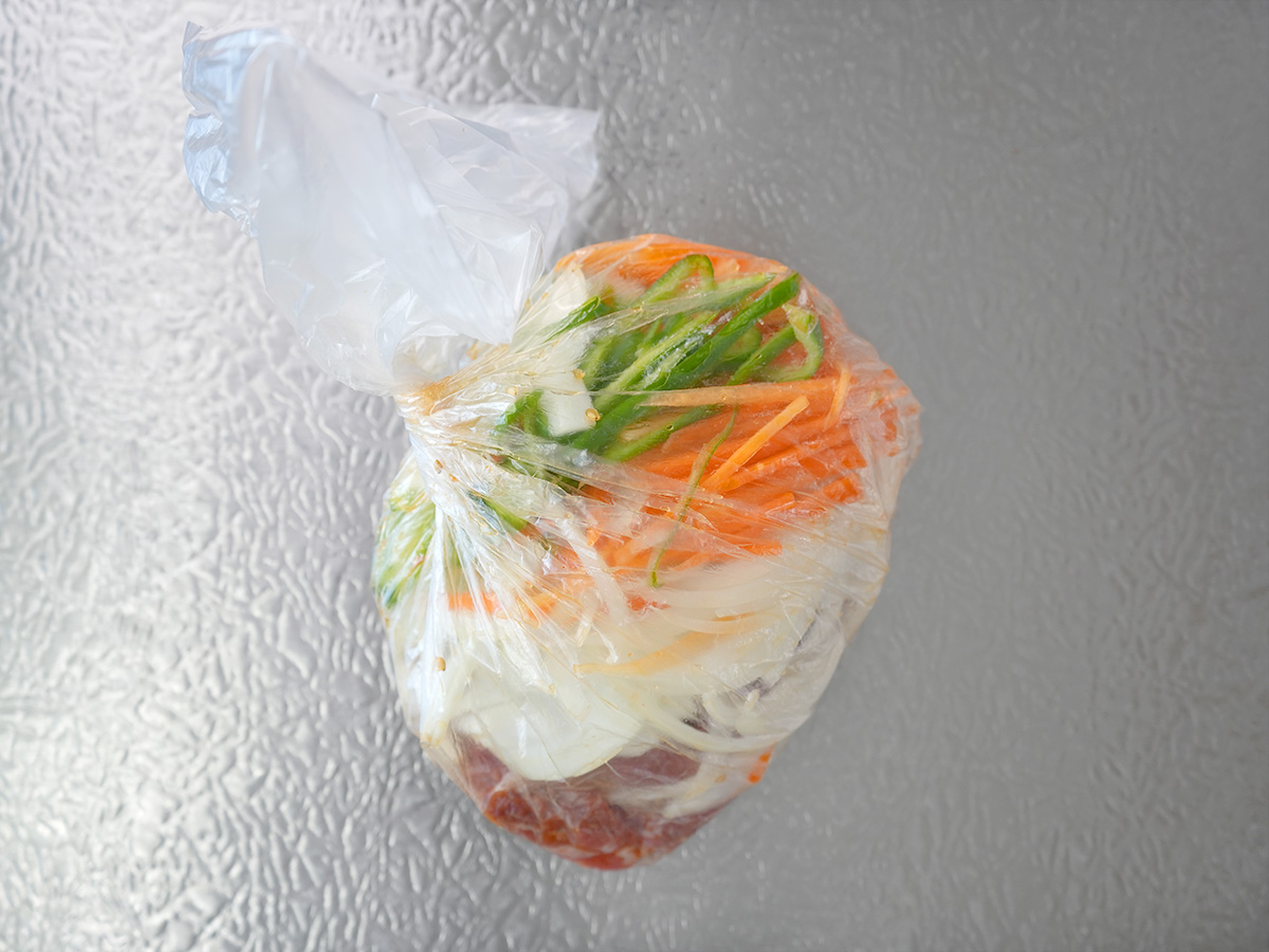 ポリ袋に切った玉ねぎ、にんじん、ピーマンを加えて口を縛るシーン