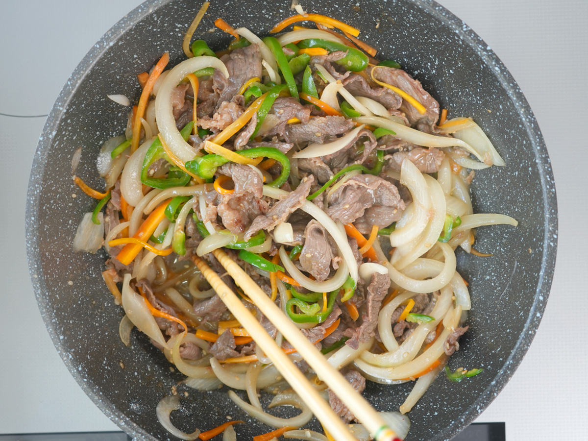 フライパンを熱し、漬け込んだ牛肉と野菜を入れて炒めるシーン