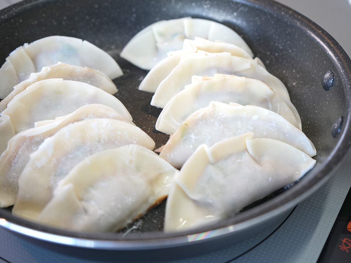 フライパンにサラダ油を熱して餃子を並べるシーン