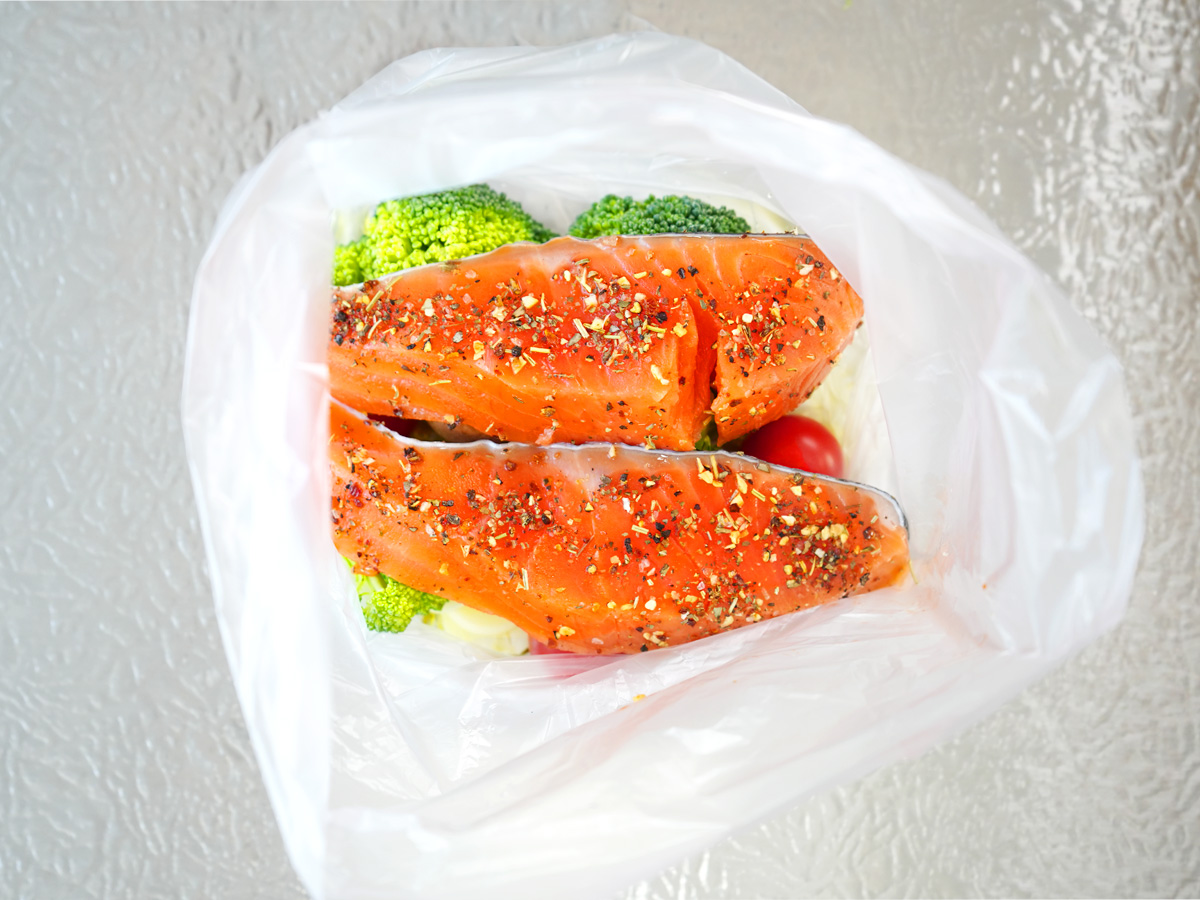 にんにく、オリーブオイル、鮭、ブロッコリー、ミニトマト、マッシュルームをポリ袋に入れるシーン