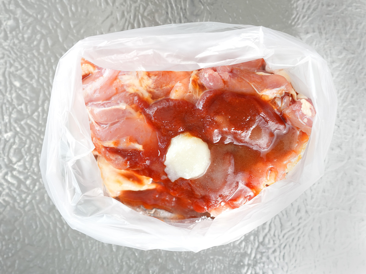 ポリ袋に鶏もも肉とAのトマトケチャップ、ソース、砂糖、酒、にんにくを入れるシーン