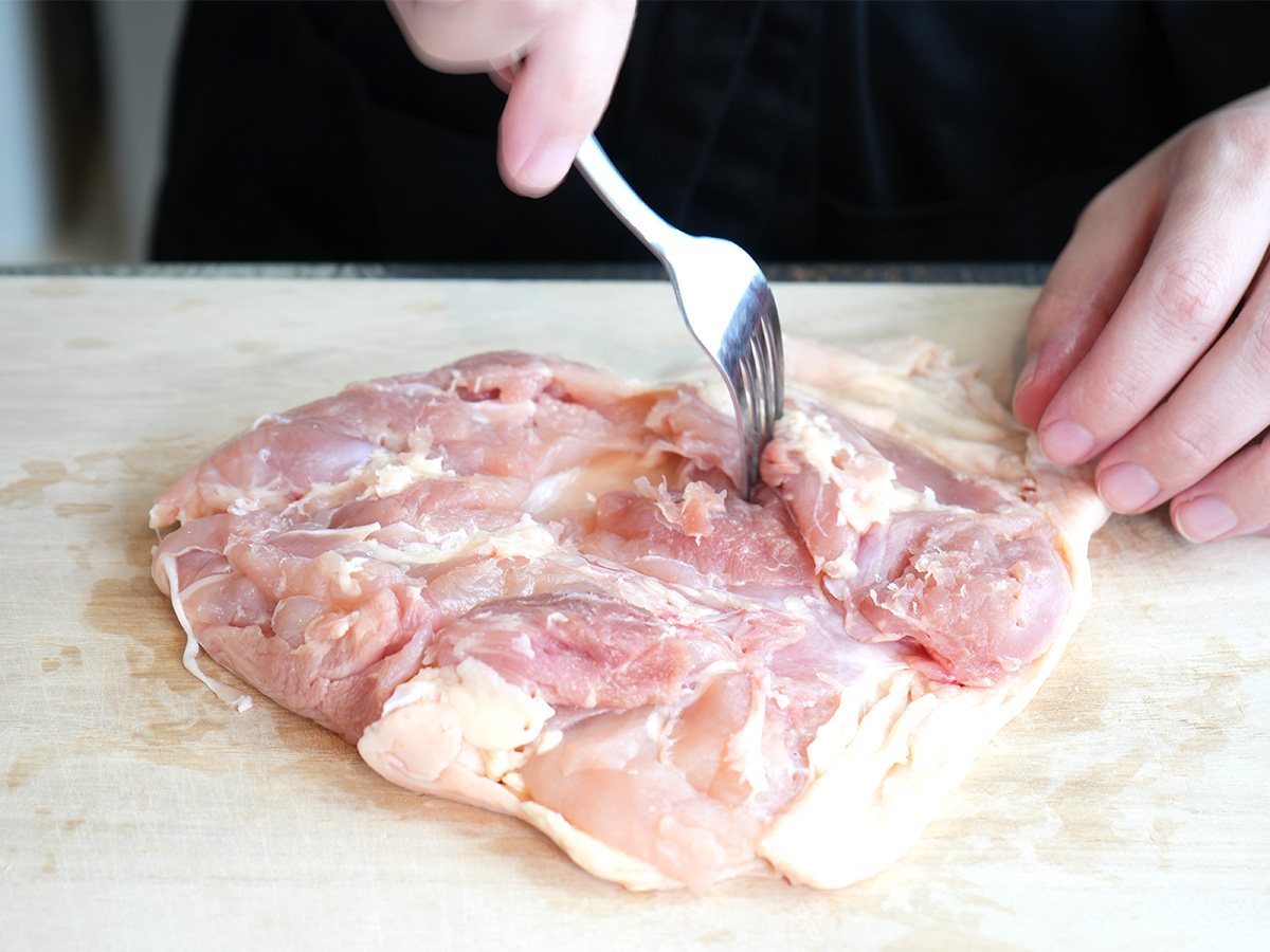 鶏肉の全体にフォークで穴を開けるシーン